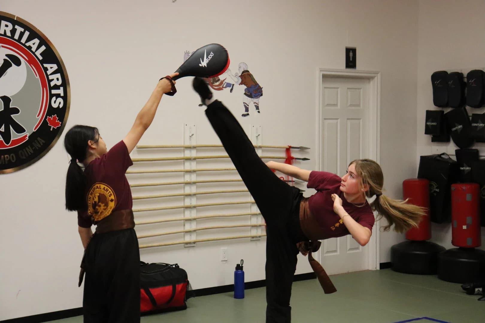 A student throwing a high kick at pads held by a partner