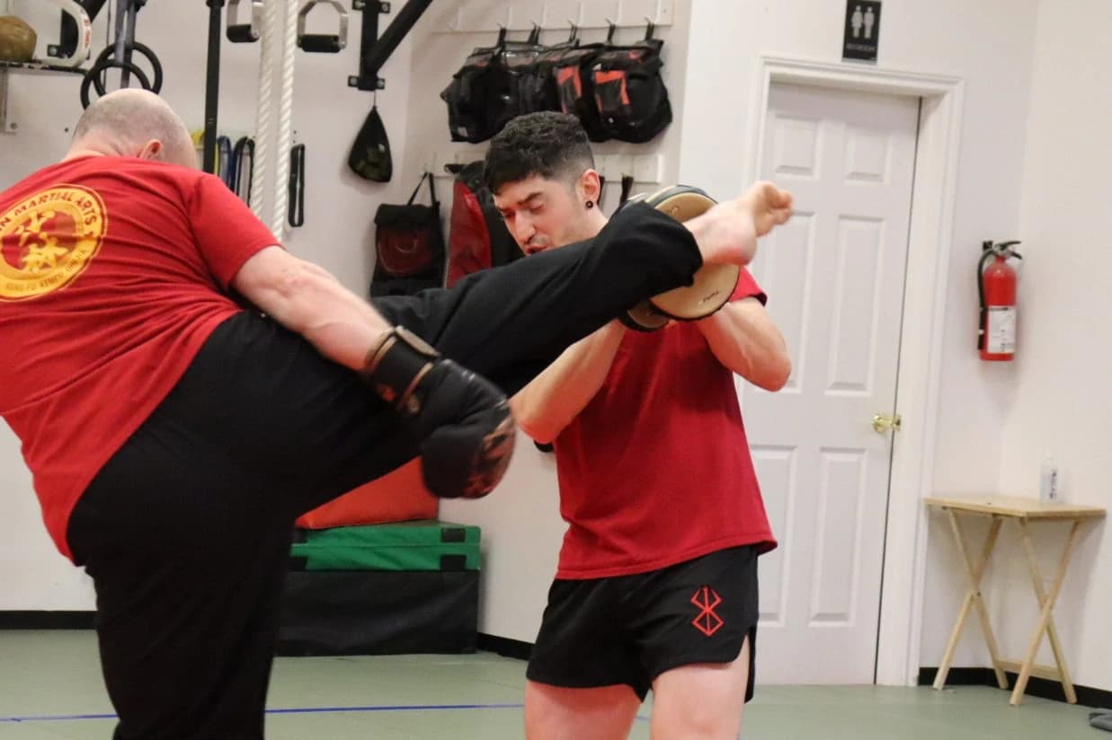 Two students practising a high kick and pad-hold drill