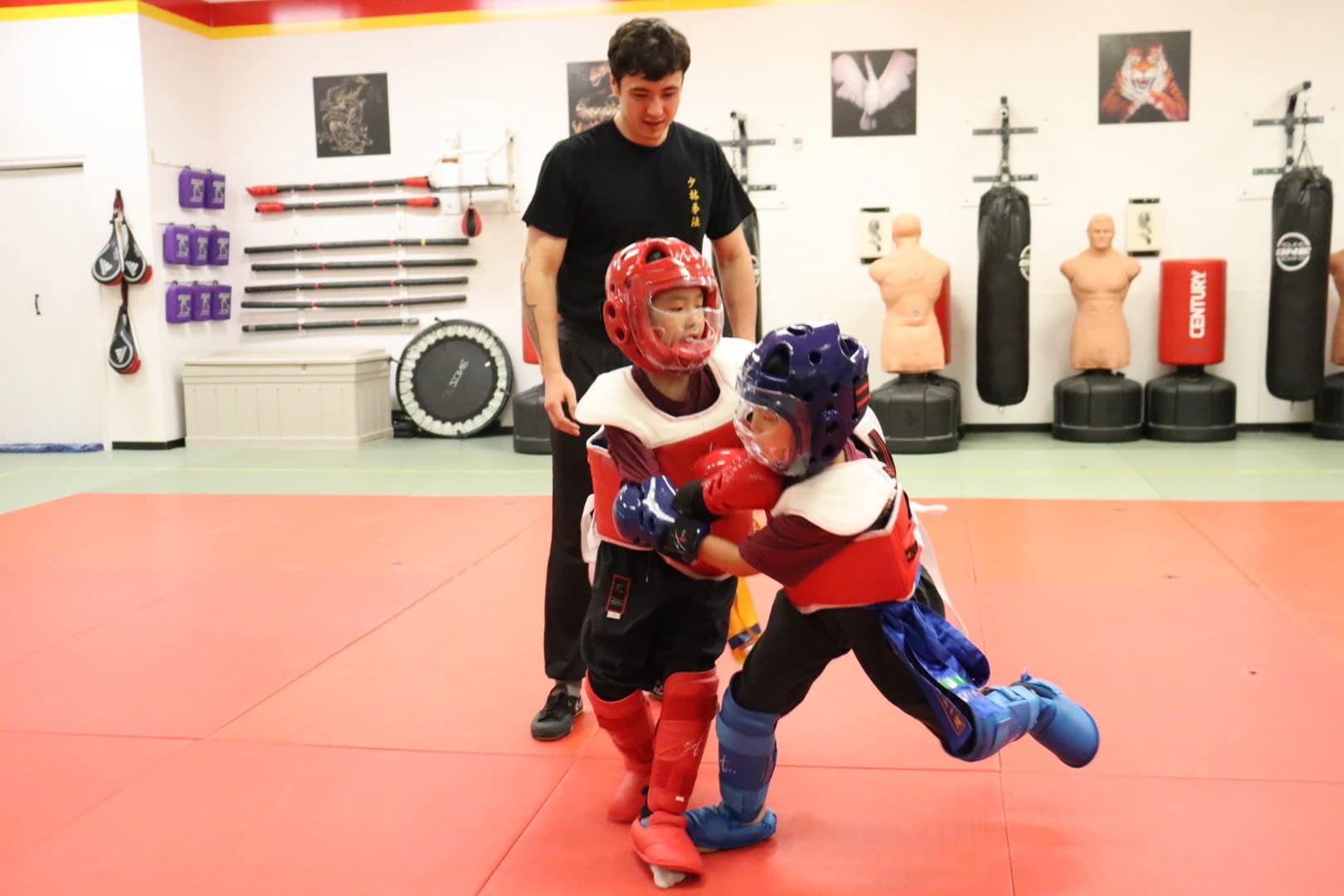 Two kids in sparring headgear practising while an instructor watches